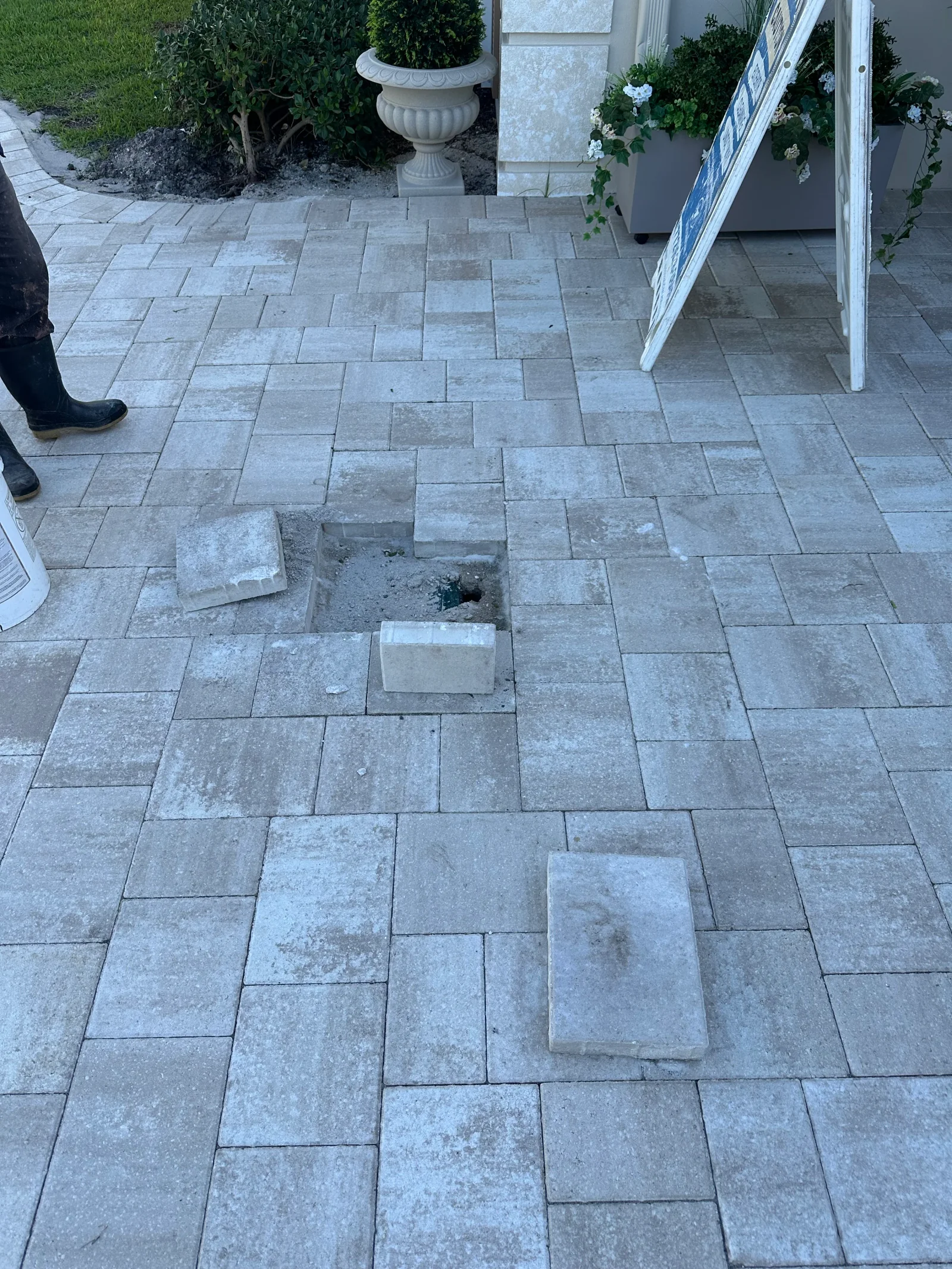Interlocking gray concrete pavers with a partially excavated section exposing sand base and removed pavers during repair