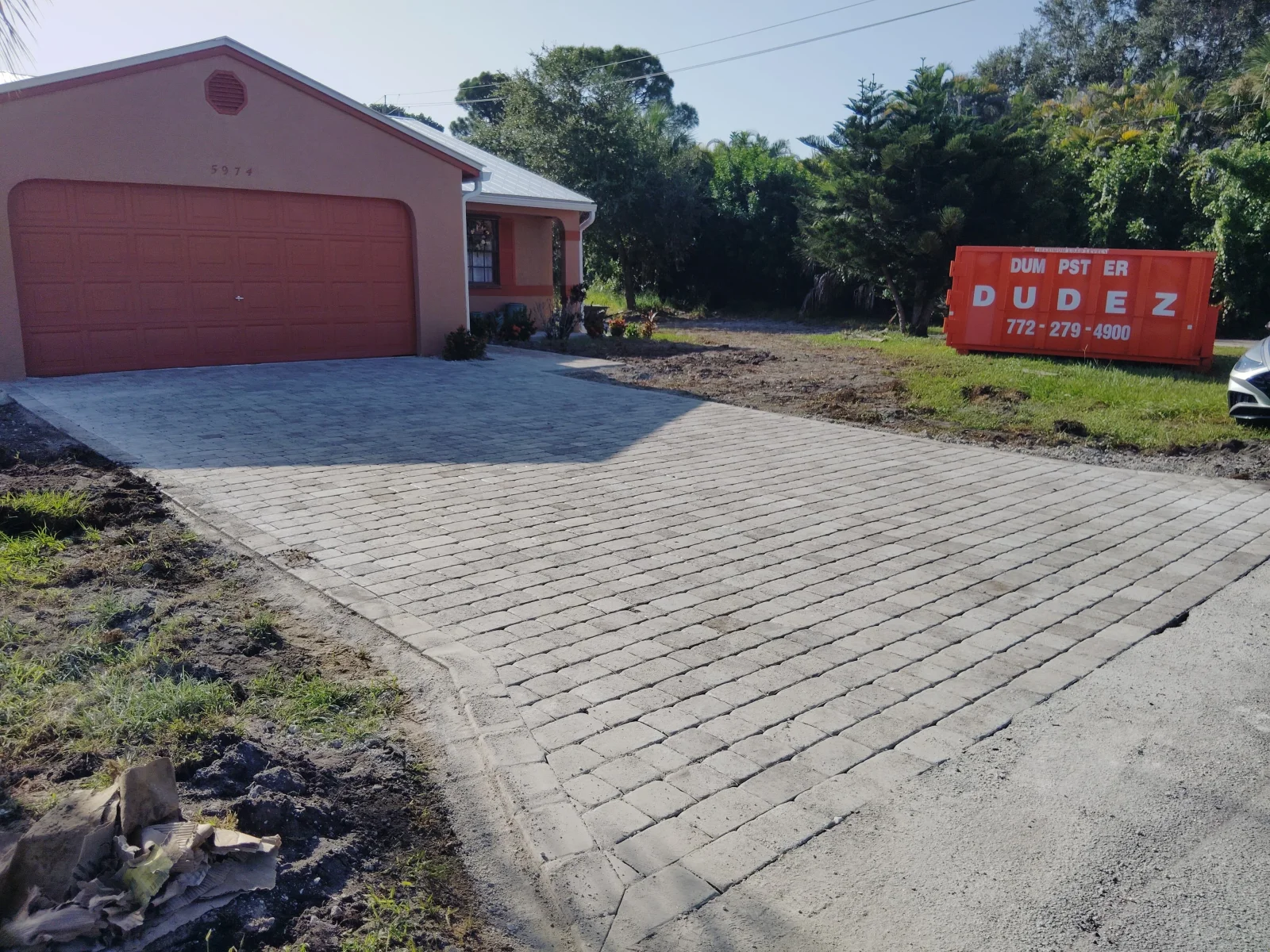 Gray interlocking concrete paver driveway with border edging beside stucco home and red garage door