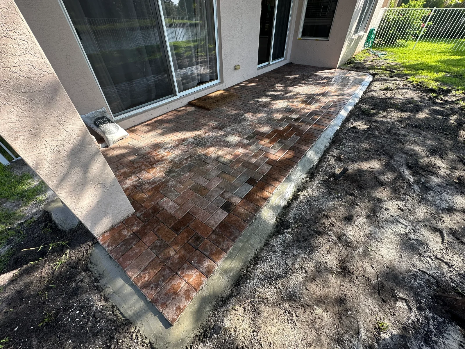 Herringbone brick paver patio with concrete edge border beside stucco wall and sliding glass doors